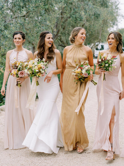 Beautiful bride walks down path holding bouquet and talking with her bridesmaids