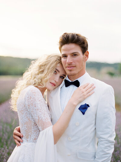 Bride rests her head on grooms shoulder while standing in lavender fields in Provence