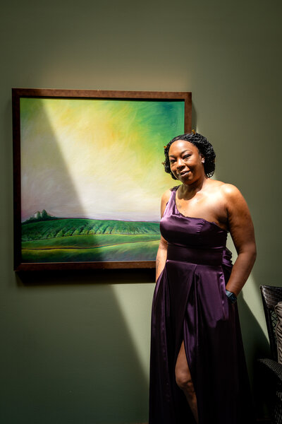 Woman in elegant purple gown posing beside modern landscape painting – photographed by wedding photographer Niko Coric – Lumen Clarity Media