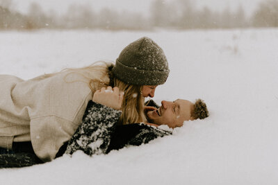 A couple hugging and rolling in the snow while they both laugh