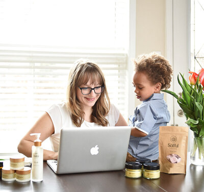 entrepreneur working on computer with her young son looking on