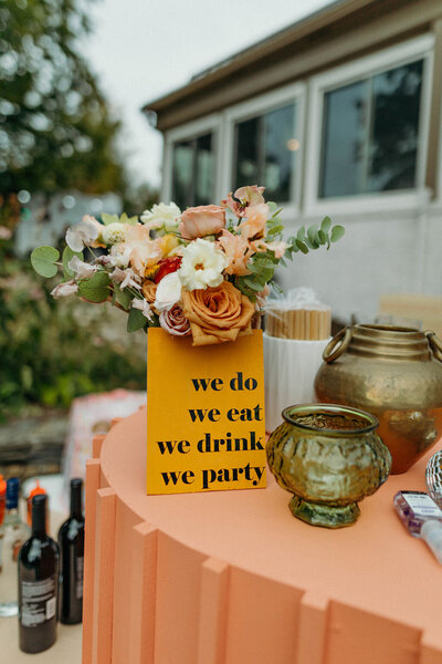 Sign on top of orange bar with flowers at wedding reception