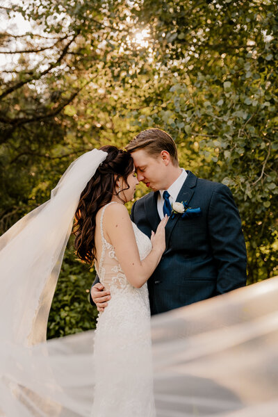 The bride and groom stand in the trees, forehead to forehead, as the veil blows in front of them. Located at Mountain Springs Lodge in Plain, Washington.