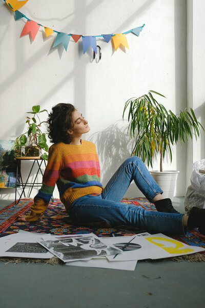 Woman in multi-colored sweater sitting on the floor, surrounded by plants