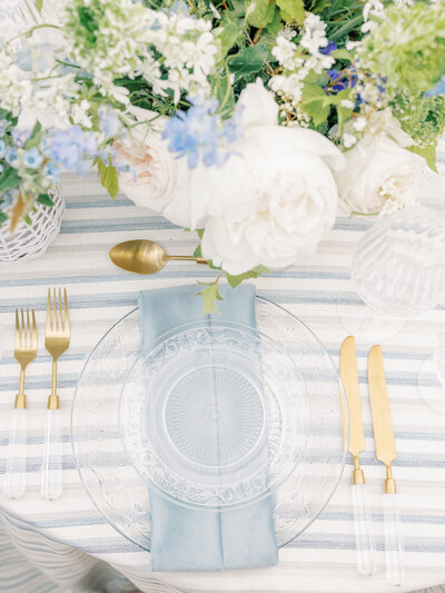 Photo from above of a light blue and gold themed table setting with blue and white floral arrangements
