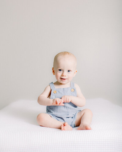 Happy baby holding his hands in a blue romper in neutral nursery by NH newborn photographer Fieldstone Studio