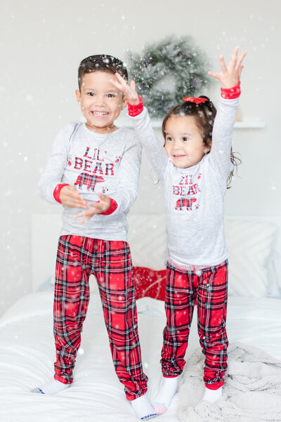 Brother and sister jumping on the bed with snow at Christmas  by Miami Christmas Mini Session Photographer MSP