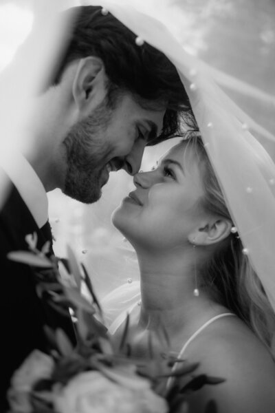 Ein schwarz-weiß Bild eines verliebten Hochzeitspaares unter einem Schleier bei ihrem Paarfotoshooting.