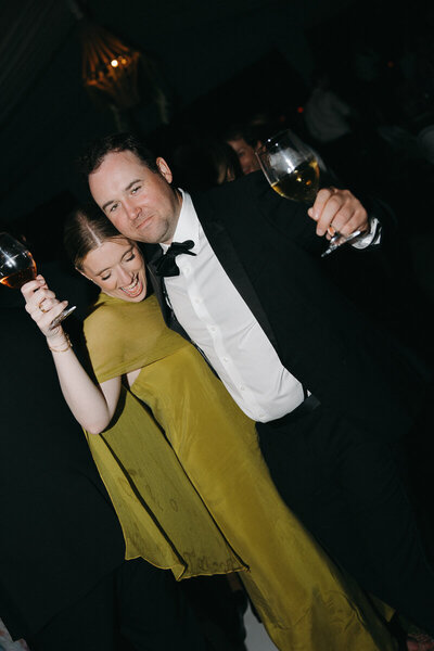 couple dressed in black tie attire holding drinks and dancing