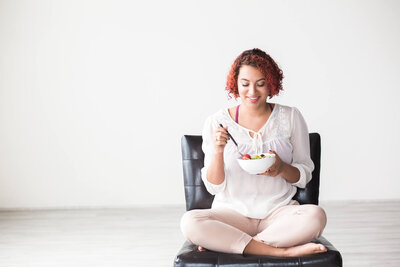 Picture of a woman smiling and eating a salad. 