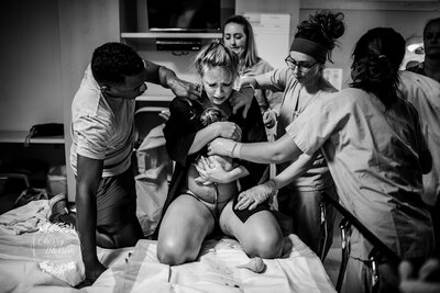 Black and white photo of a woman holding a newborn baby surrounded by doulas