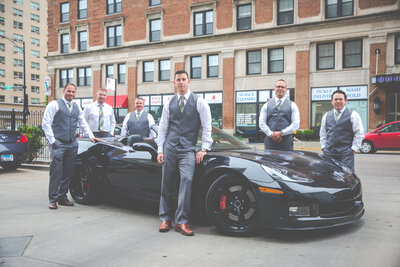 Groomsmen in gray tuxedos pose in front of a sport car in downtown Chicago.