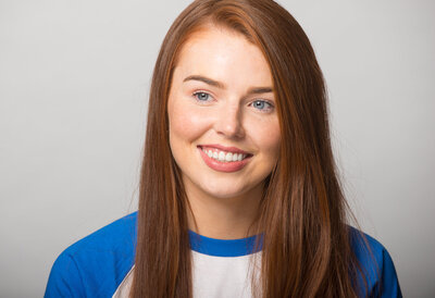 Headshot of woman with red hair wearing white and blue top top
