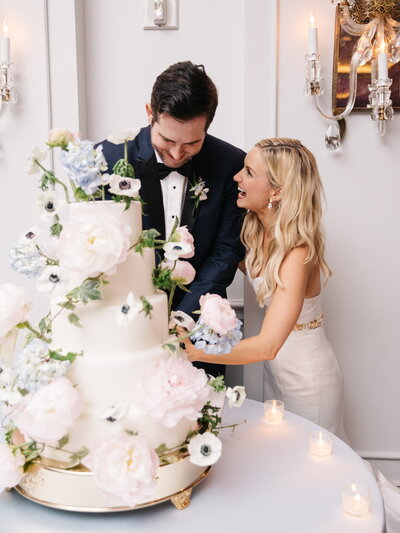 Bride and groom laugh as they cut their wedding cake with wired flowers