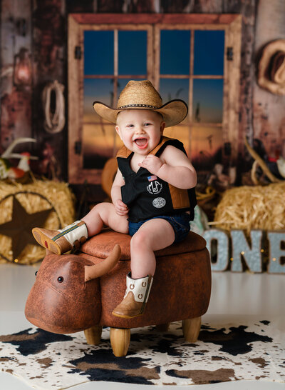 A one year old cowboy celebrates his first birthday while sitting on a stuffed bull.