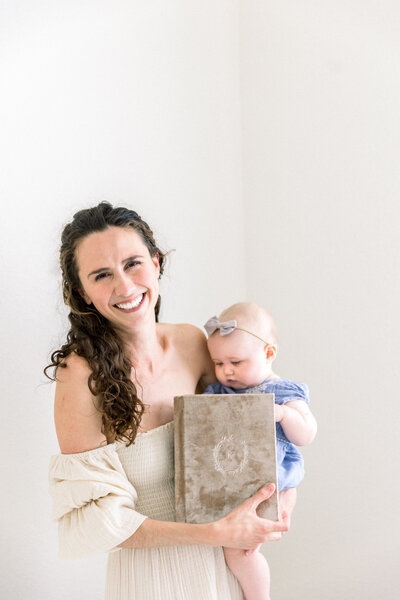 photo of Kelsey Krall Sacramento Family Photographers holding album and baby and smiling at the camera