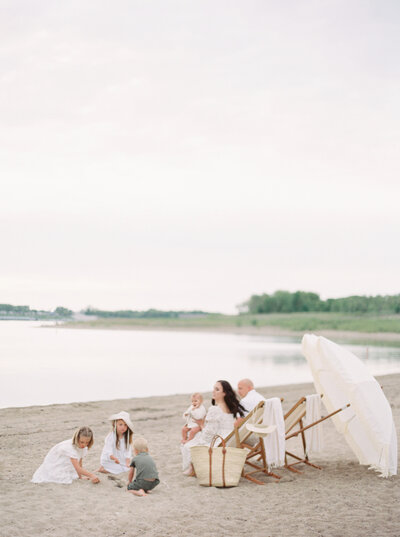 Family playing on beach sitting in chairs white umbrella Denver Family Photographer