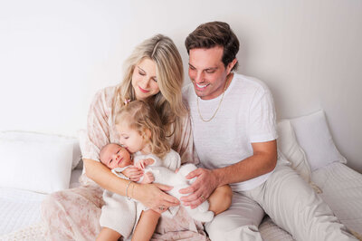 A older sister in her parents arms kissing her new baby brother in Raleigh NC area photographer studio.