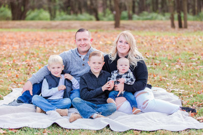 Mother and father sit on a picnic blanket and smile with their 3 young boys