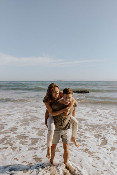 man giving woman piggyback ride on the beach