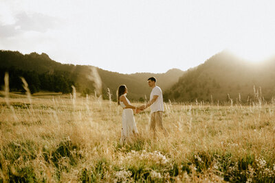 A couple holding hands in a field at sunset with mountains in the distance