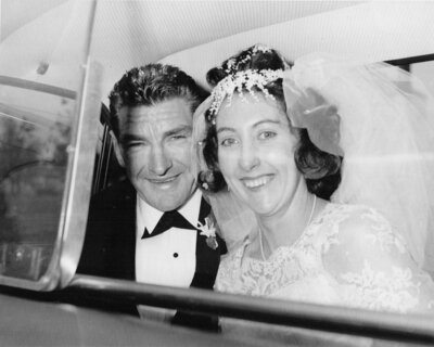67 year old wedding photo of bride and groom in the back of a car smiling at the camera in black and white.