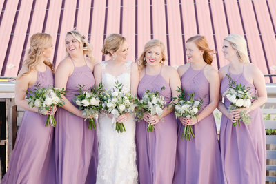 Bride and her bridesmaids in lavender smile and hold bouquets