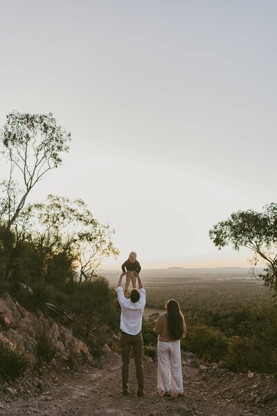 Outdoor family photography session at sunset with parents and child walking along a hilltop.