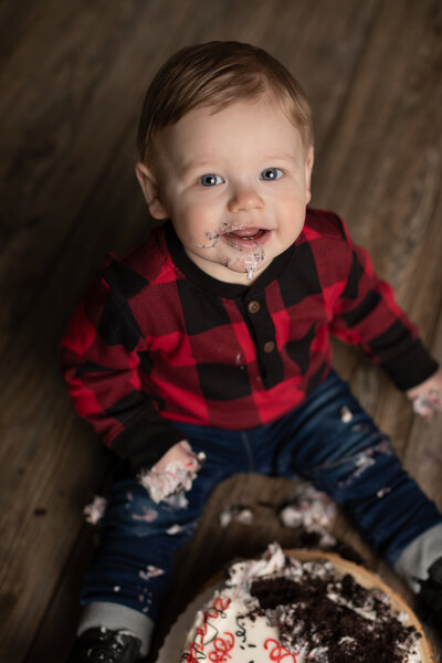 one year old boy in red plaid shirt eating cake for cake smash photoshoot