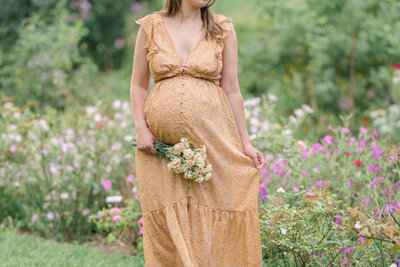 A pregnant mother holds a bouquet of flowers near her bump.