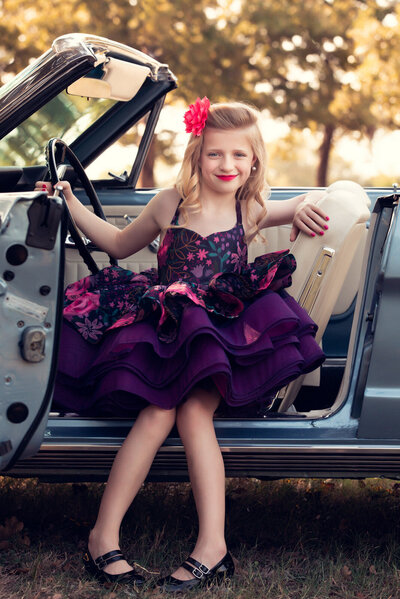 girl-in-purple-floral-dress-sitting-with door open-in-convertable