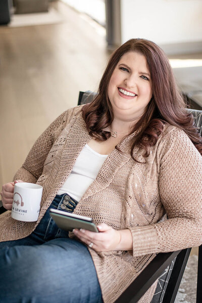 Julia Levine, The Podcast Teacher, smiling and holding a cup of tea and a kindle