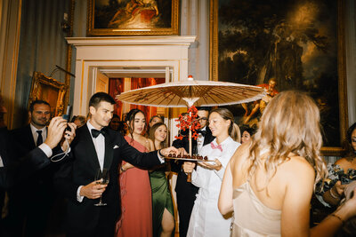 Guests at a sophisticated black-tie party in London enjoying a traditional sweet treat served beneath a Chinese parasol.