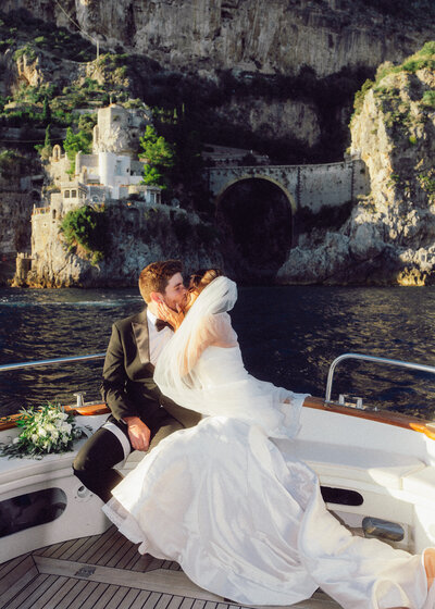 Bride and groom embracing on a boat along the Amalfi Coast, captured in soft film tones.