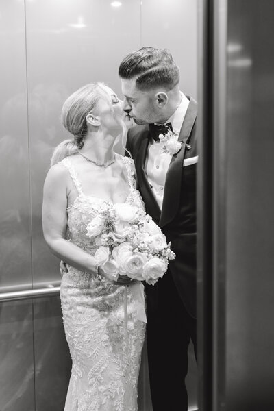 Bride and groom kissing in an elevator, bride wearing Wtoo by Waters gown holding white roses flower bouquet, groom wearing Tom Ford suit in black color,black and white fine art wedding photography, photo by Anastasiya Photography - San Francisco Wedding Photographer
