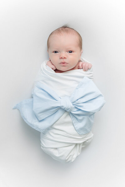 Baby boy in a blue bow swaddle  against a white studio backdrop
