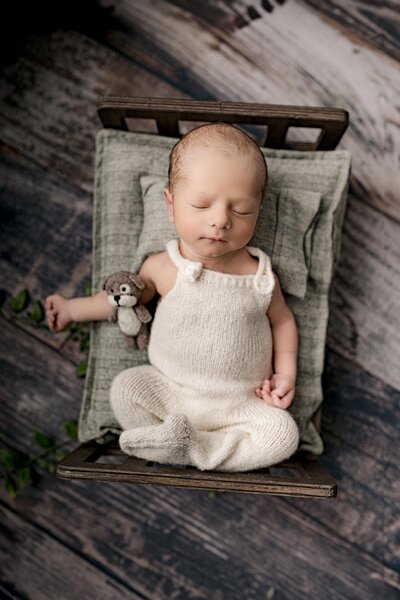newborn baby boy lays on bed dressed in cream knit outfit with a stuffed puppy beside him