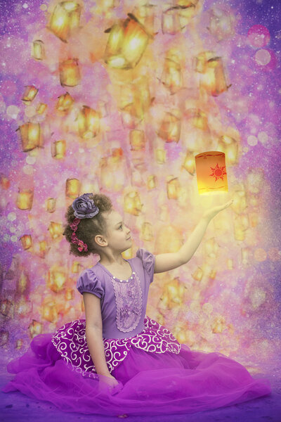 Girl in a purple puffy dressing sitting on the ground with her left arm in the air, above it a lantern floats shining light below it. Behind the girl i sa purple background lit up with golden lanterns floating everywhere