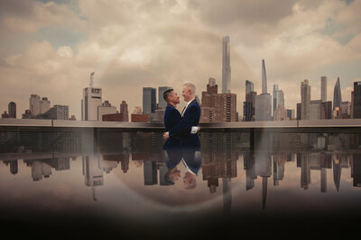 Two grooms with their arms around each other with a city skyline behind them.