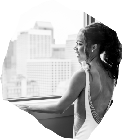 Black and white photo of bride in low-back dress looking out over city skyline - professional photo edit by Uncut Gems