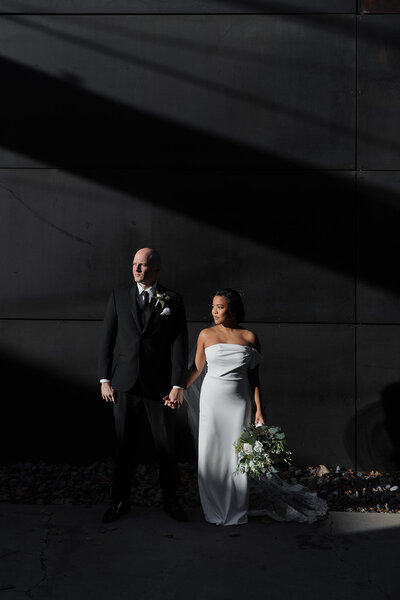 wedding couple stands bathed in late day sunlight in front of a dark wall