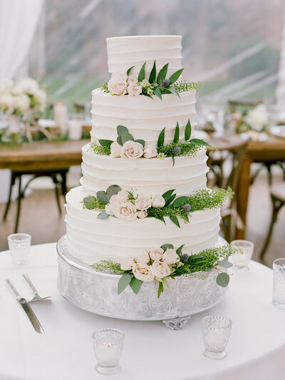 White tiered-wedding cake decorated with small pink flowers and green leaves