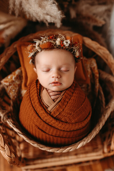 Newborn baby girl wearing a fall themed flower crown and wrapped in an orange blanket.