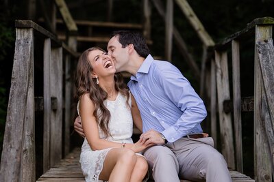 engaged couple laughing and kissing seated on wooden steps girl in white dress man in blue button down