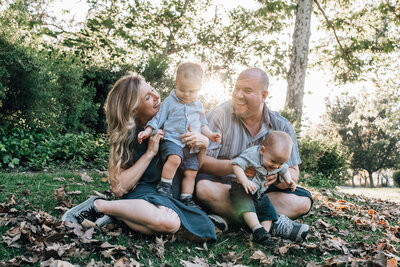 Happy family with twin toddlers sit in grass at sunset