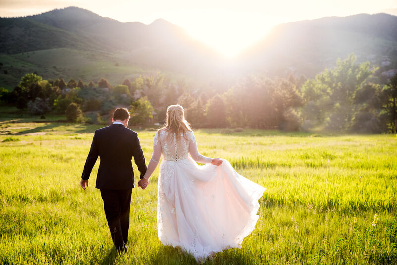 A bride and groom walk away from the camera in a field at golden hour at The Manor House in Littleton, Colorado.