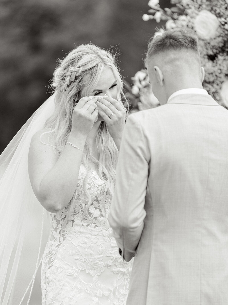 Black and white photo of bride and groom at the altar while bride wipes her tears