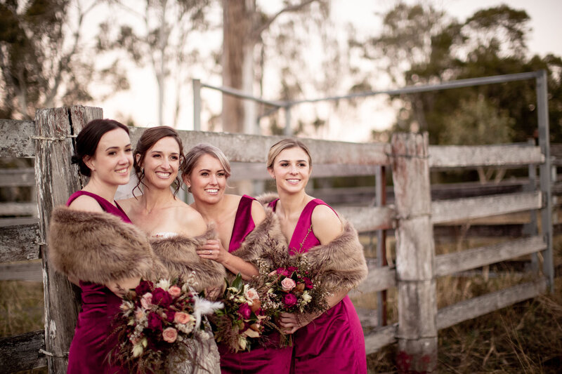 Bride and Bridesmaids taking a pose at the farm fence with their bouquet of flowers