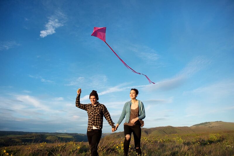 a man and woman fly a kite while running through the grass
