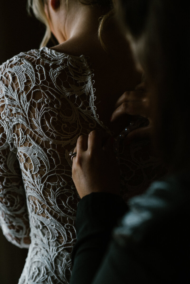 Bride having lace wedding dress buttoned up at the back